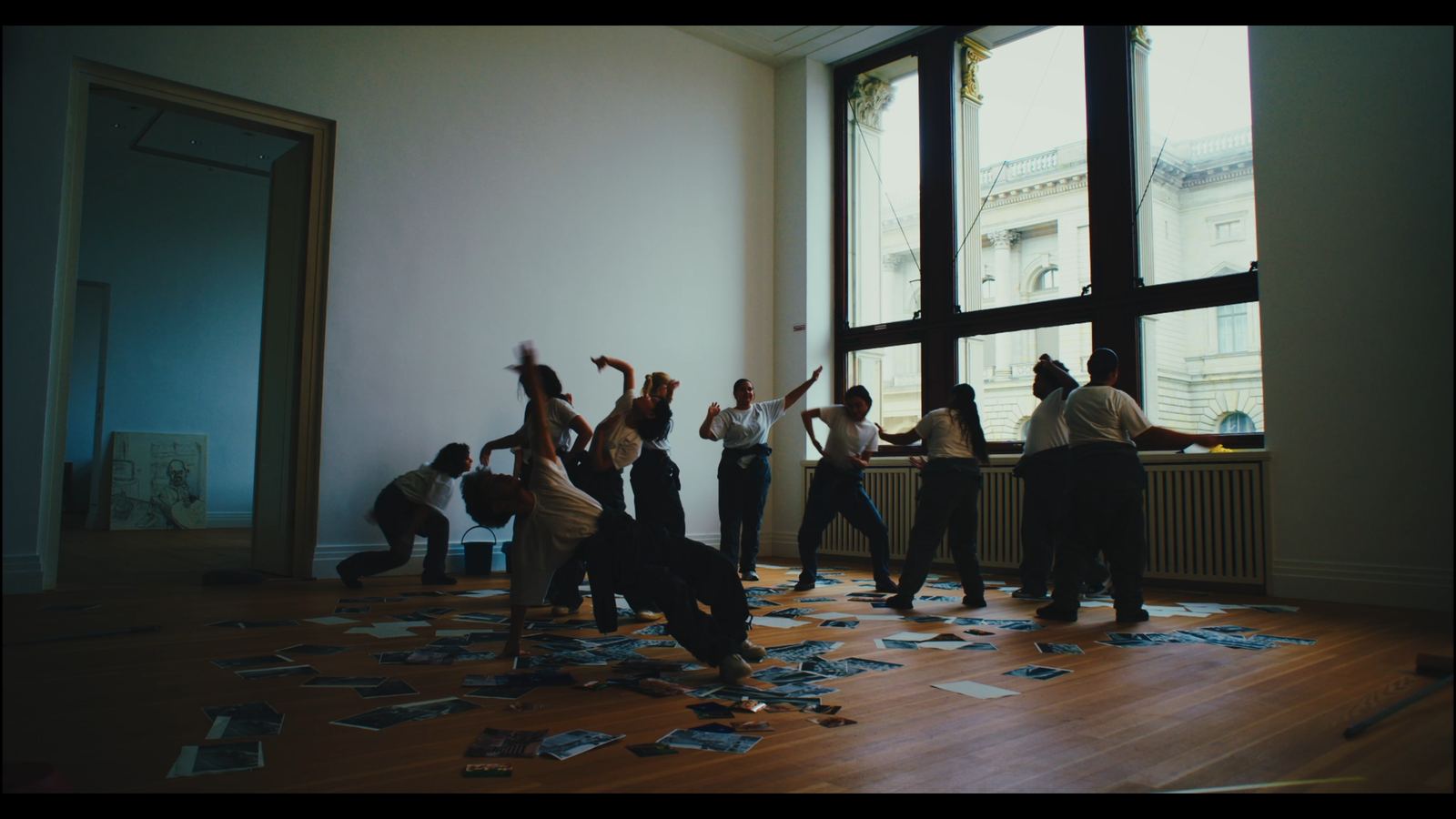 Dream Baby Dream — performers on a sunlit floor of scattered photographs