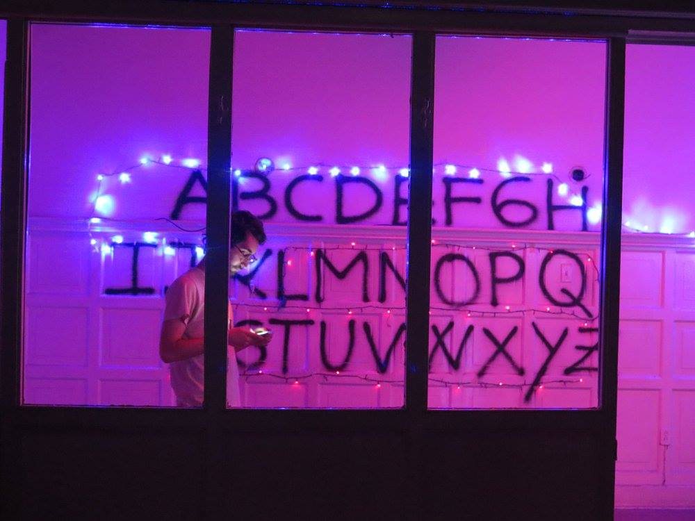 Alphabet painted on a wall with fairy lights, Stranger-Things style, figure behind the glass
