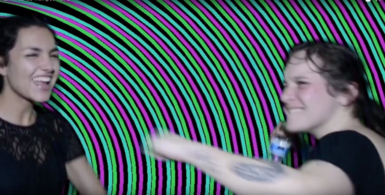 Two people laughing in front of a spinning green and magenta spiral projection