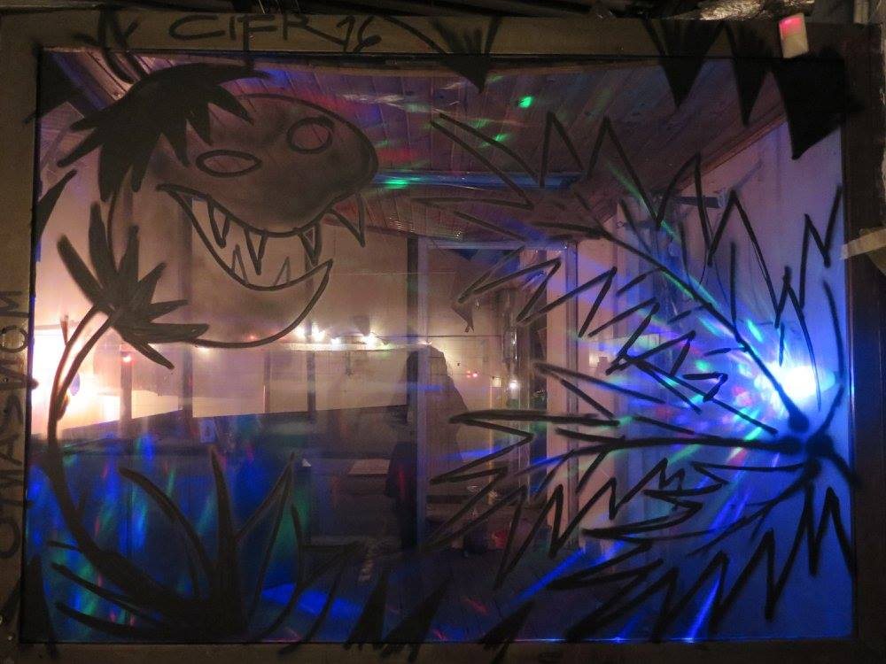 Window painted with a black monster and jungle motifs, colored lights behind