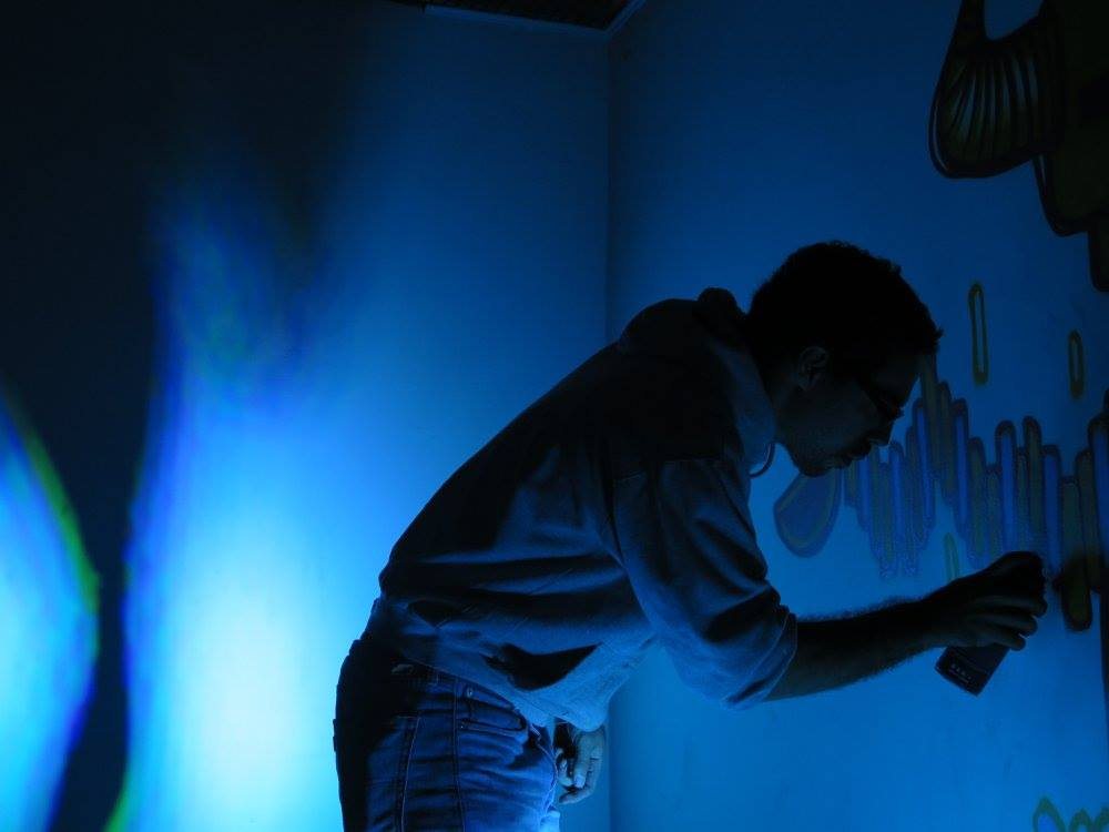 Artist spray-painting a UV mural on the wall during set-up