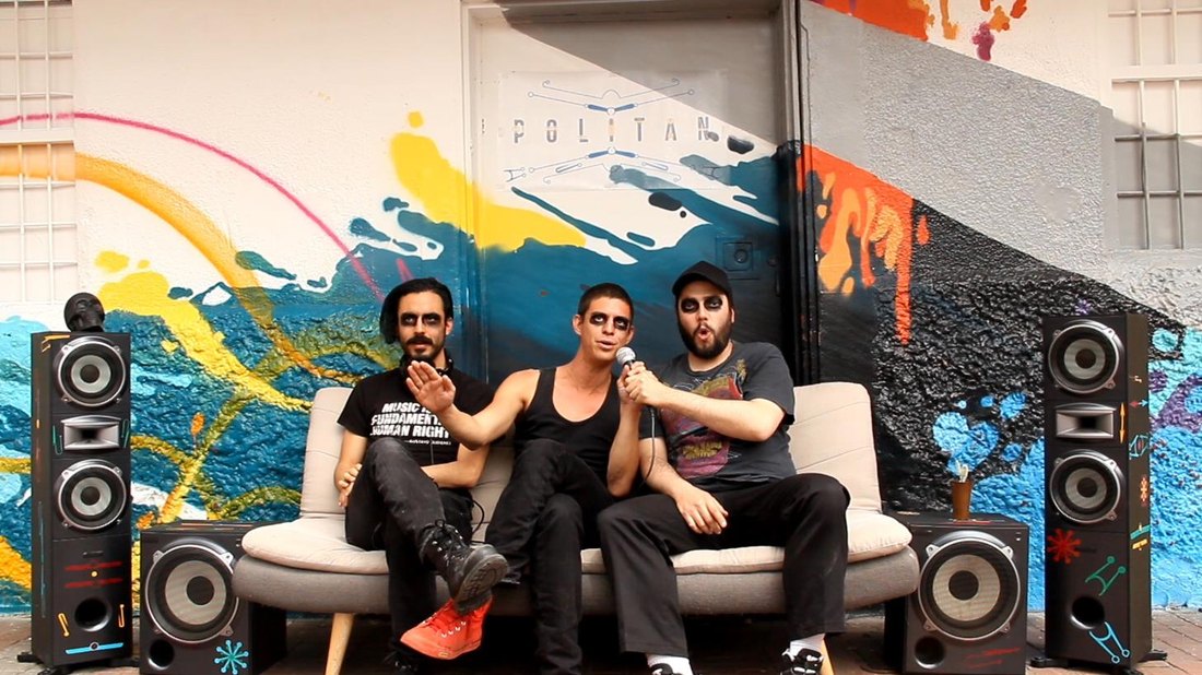 Still from the Politan Kickstarter video — the band on the couch under the Politan logo