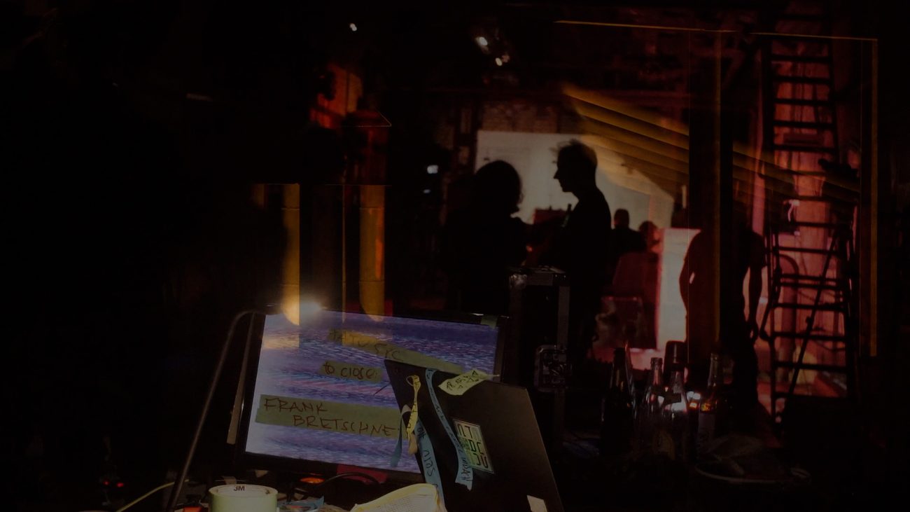 T.A.T.V. — silhouettes and a performer's screen in the dark venue