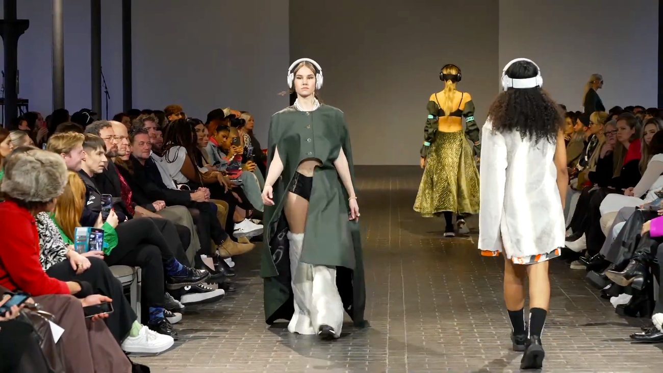 WE.4 runway — model in a green cape with headphones